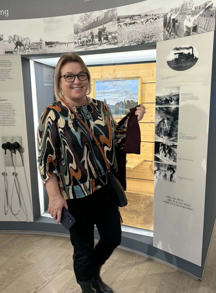 Kobieta stoi przy planszach z archiwalnymi fotografiami i opisami (kliknięcie powiększy zdjęcie)