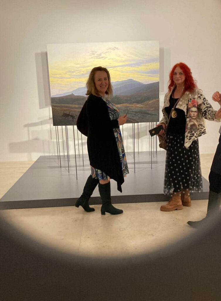 Dwie osoby stoją przed obrazem przedstawiającym krajobraz i pozują do zdjęcia (kliknięcie powiększy zdjęcie)