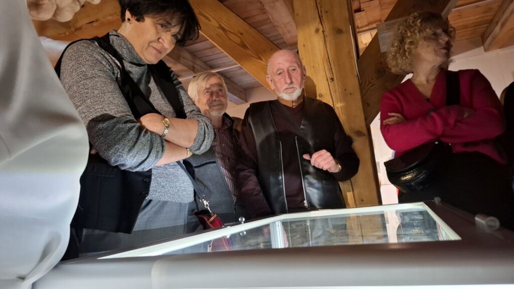 Zwiedzający pochylający się nad podświetloną gablotą z eksponatami w drewnianej przestrzeni wystawowej (kliknięcie powiększy zdjęcie).