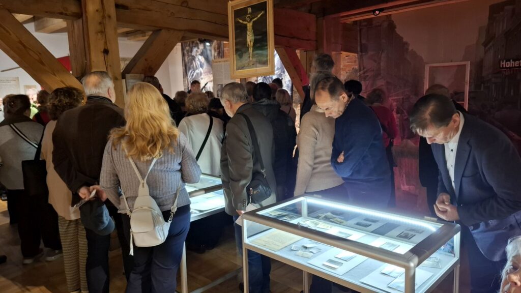 Zwiedzający oglądający dokumenty i fotografie w podświetlonej gablocie muzealnej (kliknięcie powiększy zdjęcie).