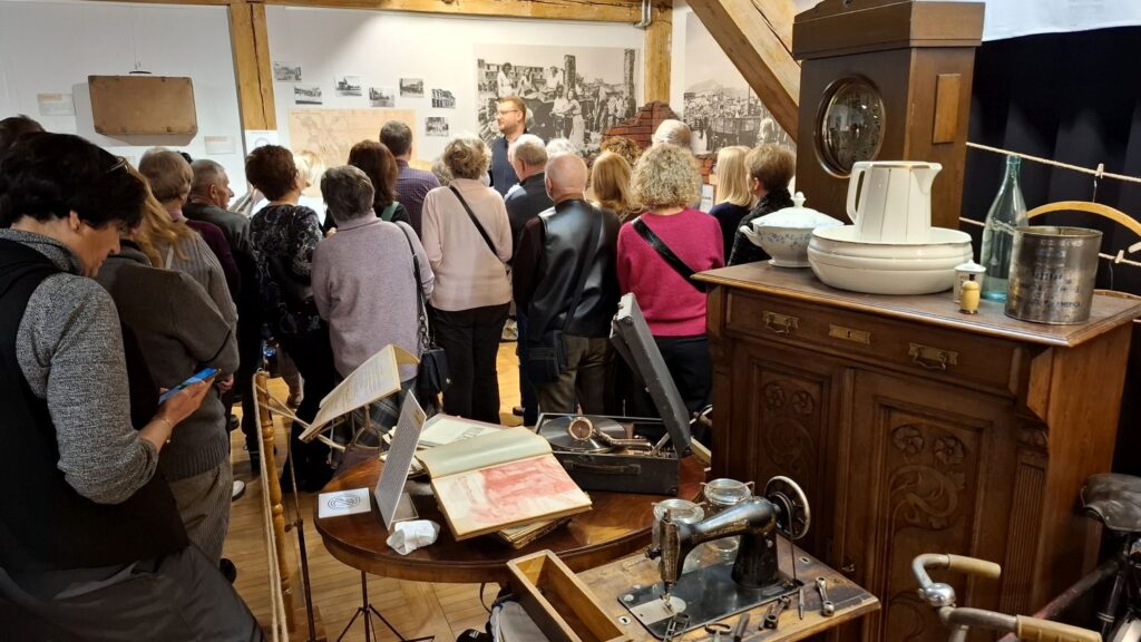 Grupa uczestników oglądająca ekspozycję dawnych przedmiotów codziennego użytku, takich jak meble, naczynia i urządzenia (kliknięcie powiększy zdjęcie).