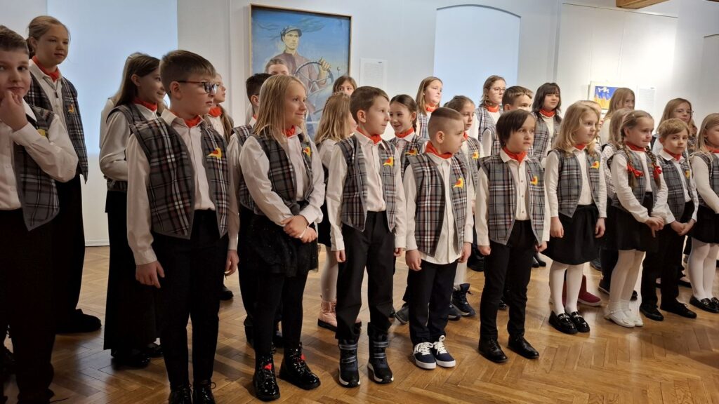 Dziecięcy chór stojący w rzędzie podczas występu w sali muzealnej, widok z boku (kliknięcie powiększy zdjęcie)