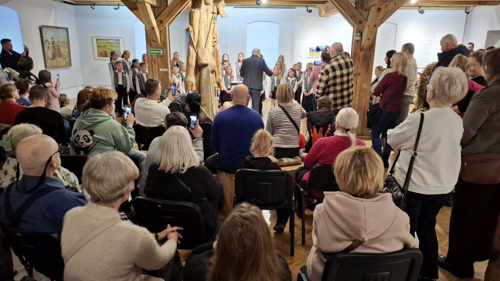 Publiczność siedząca i stojąca w sali muzealnej podczas koncertu dziecięcego chóru (kliknięcie powiększy zdjęcie)