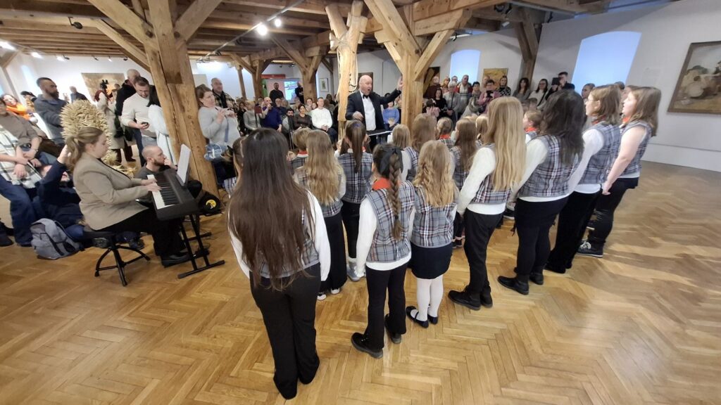 Widok od tyłu na dziecięcy chór oraz publiczność zgromadzoną w sali muzealnej podczas koncertu (kliknięcie powiększy zdjęcie)