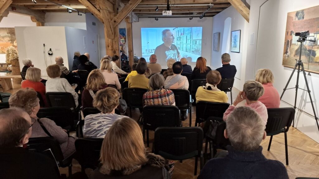 Uczestnicy wydarzenia siedzący na krzesłach i oglądający prezentację wyświetlaną na ekranie (kliknięcie powiększy zdjęcie)