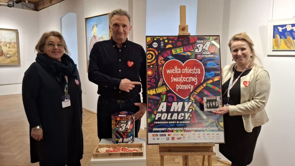 Trzy osoby pozujące przy sztaludze z plakatem wydarzenia, w tle widoczne obrazy na ścianach (kliknięcie powiększy zdjęcie)