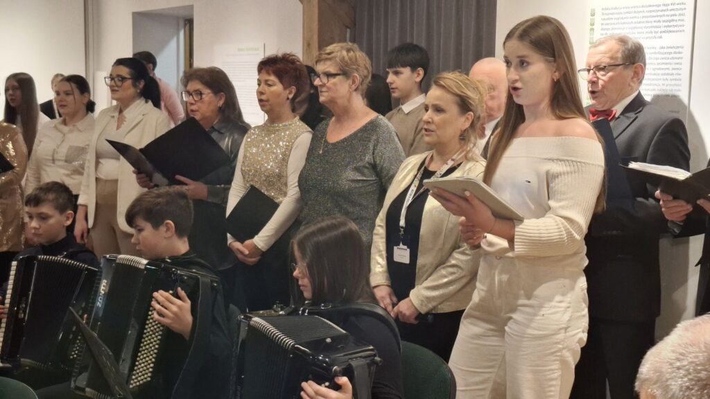 Fragment chóru z widocznymi śpiewakami i akompaniującymi muzykami siedzącymi przed nimi (kliknięcie powiększy zdjęcie)