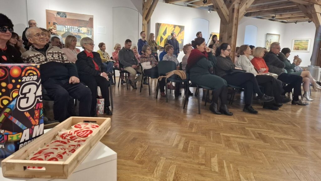 Publiczność siedząca w sali wystawowej i słuchająca koncertu chóralno-instrumentalnego (kliknięcie powiększy zdjęcie)