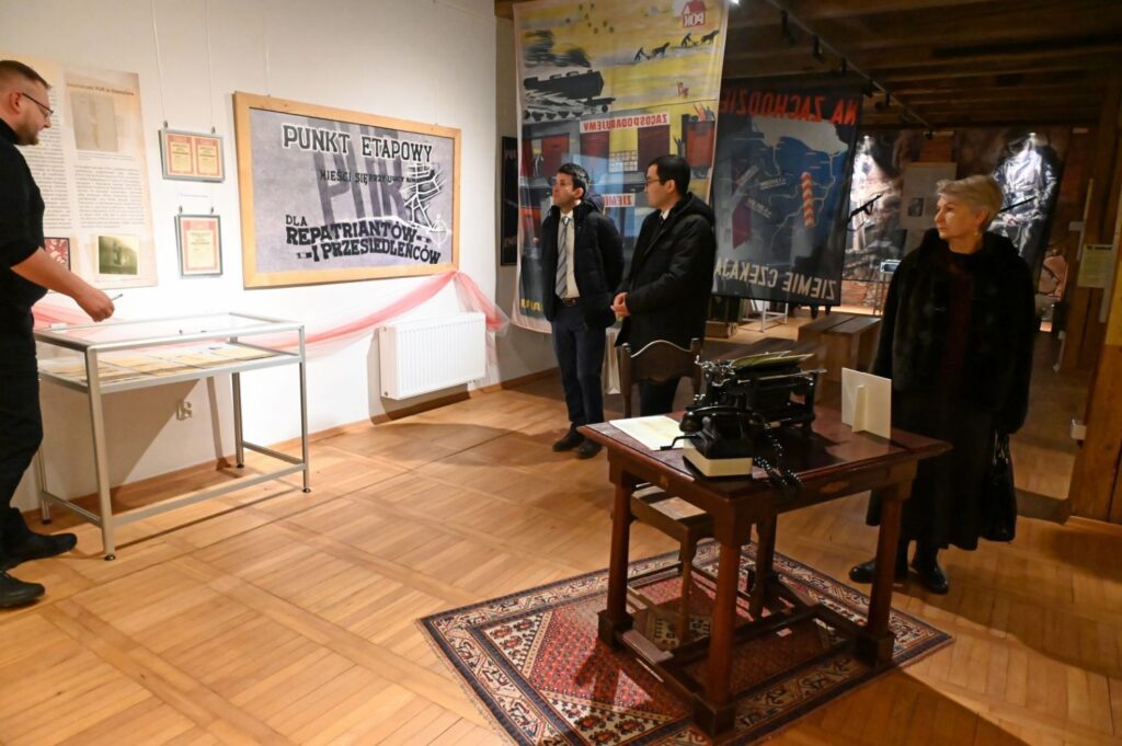 Uczestnicy oprowadzania w sali wystawowej z eksponatami historycznymi i planszami informacyjnymi (kliknięcie powiększy zdjęcie).