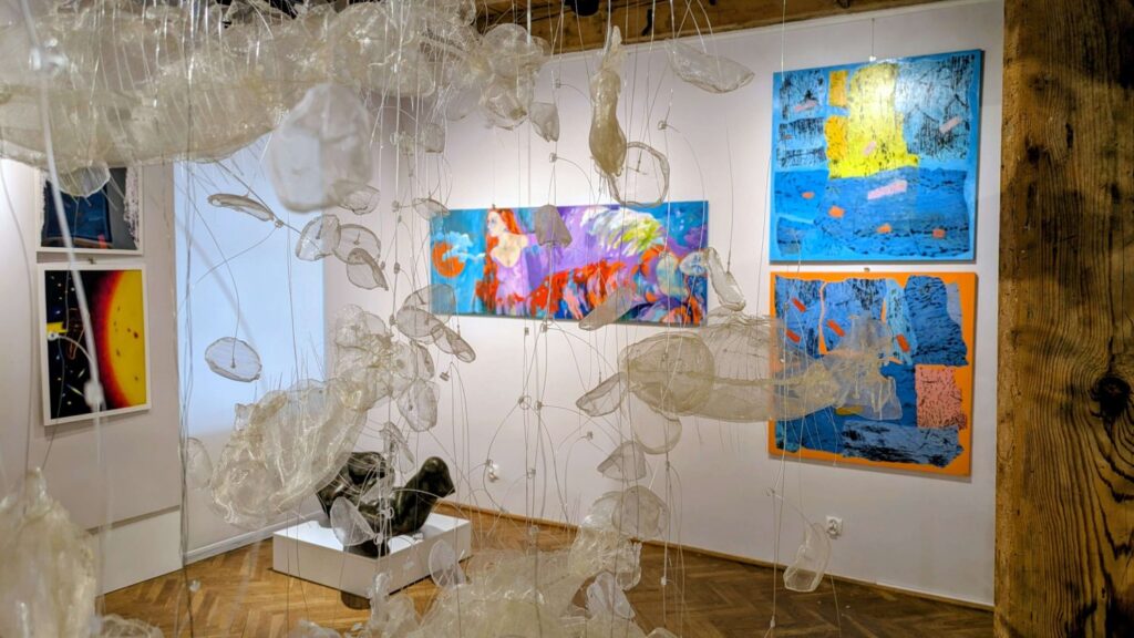 Instalacja z przezroczystych form zawieszonych w przestrzeni oraz kolorowe obrazy na ścianie galerii (kliknięcie powiększy zdjęcie).