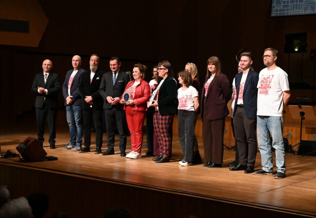 Laureaci i organizatorzy stoją w rzędzie na scenie podczas uroczystej gali wręczenia nagród (kliknięcie powiększy zdjęcie).
