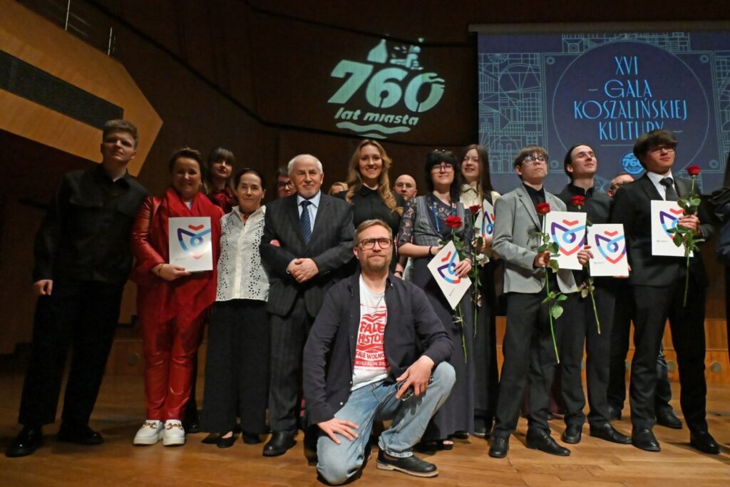 Grupa nagrodzonych osób z dyplomami pozuje do wspólnego zdjęcia na scenie na tle napisu Gali Koszalińskiej Kultury (kliknięcie powiększy zdjęcie).