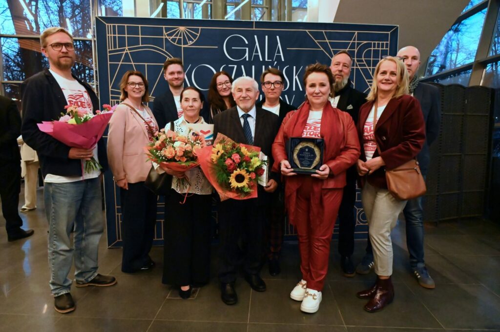 Laureaci wraz z osobami towarzyszącymi pozują do zdjęcia, trzymając bukiety kwiatów i nagrody (kliknięcie powiększy zdjęcie).