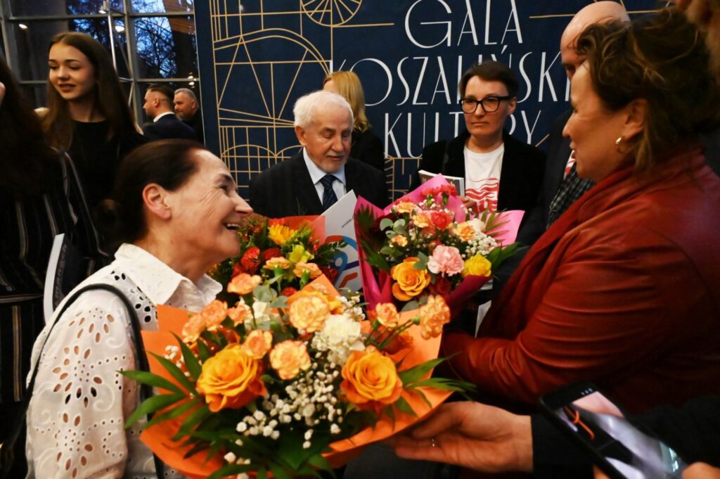 Uczestnicy gali rozmawiają po wręczeniu nagród, w rękach trzymają kolorowe bukiety kwiatów (kliknięcie powiększy zdjęcie).