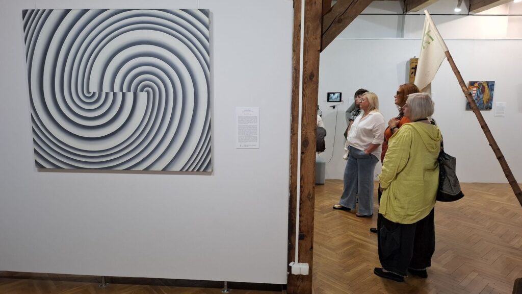 Zwiedzający zatrzymują się przed abstrakcyjnym reliefem o spiralnym układzie linii, oglądając jedno z dzieł prezentowanych na wystawie sztuki współczesnej (kliknięcie powiększy zdjęcie).