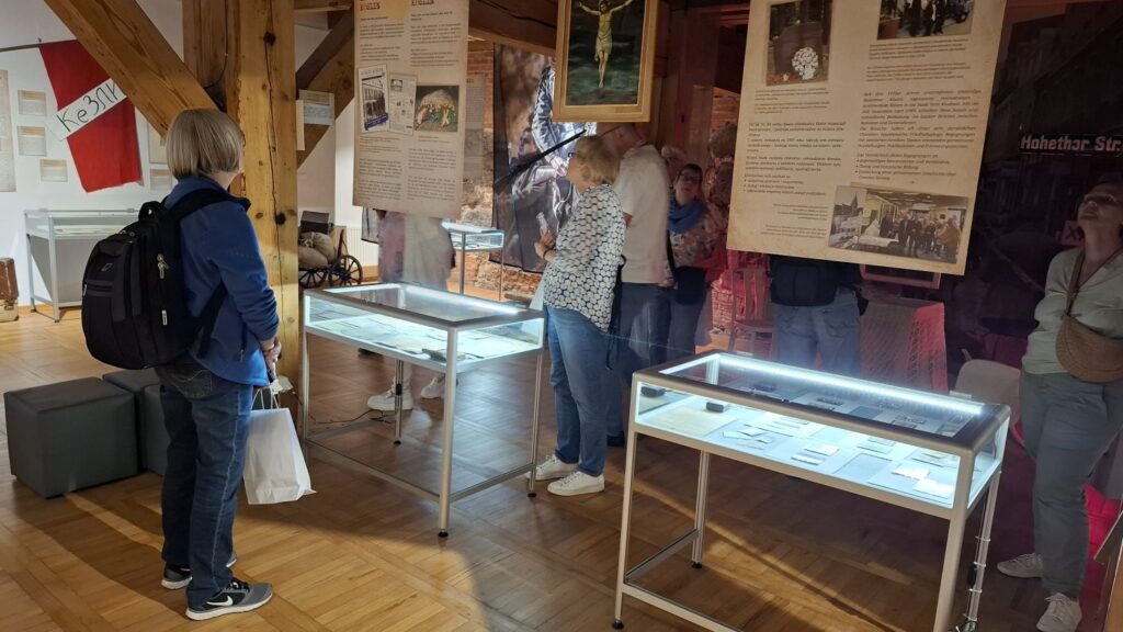 Zwiedzający przechodzą przez salę wystawową z gablotami i planszami opisującymi historię regionu (kliknięcie powiększy zdjęcie).