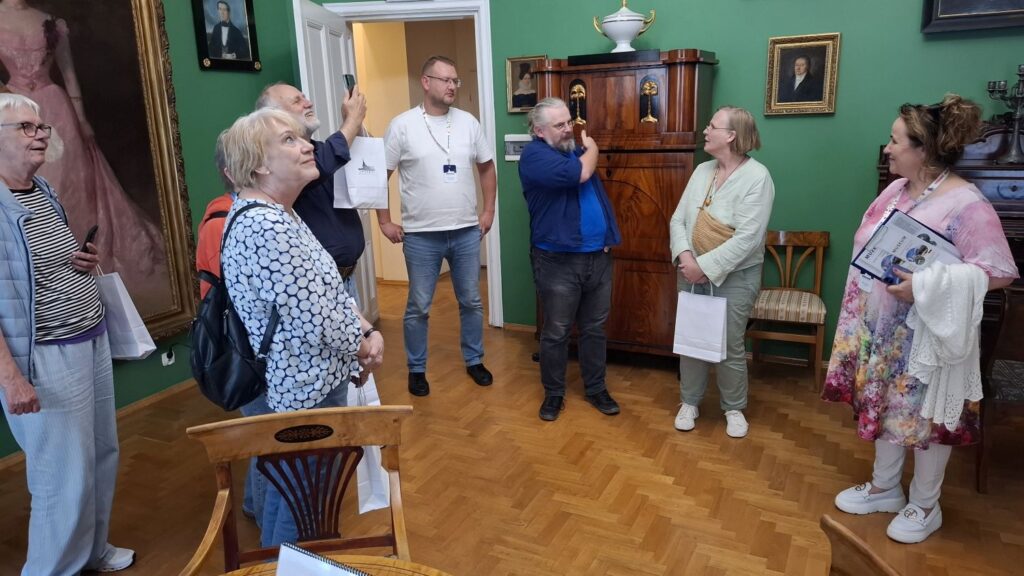 Przewodnik opowiada grupie zwiedzających o wyposażeniu zabytkowego wnętrza z portretami i meblami z XIX wieku (kliknięcie powiększy zdjęcie).