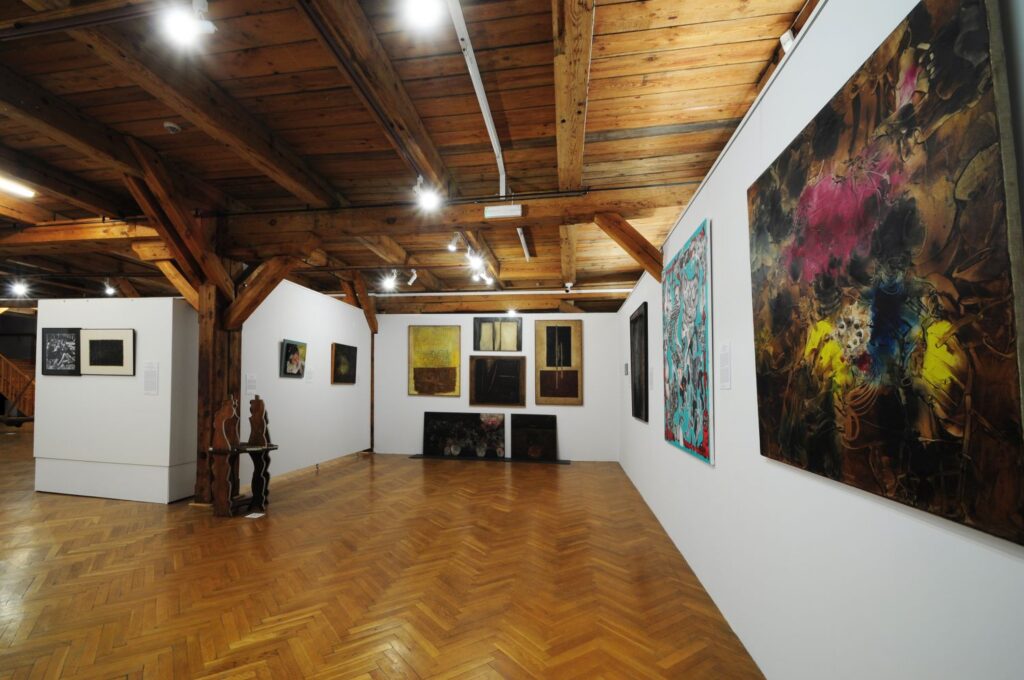 Sala ekspozycyjna z wielkoformatowymi obrazami współczesnych artystów prezentowanymi na białych ścianach galerii (kliknięcie powiększy zdjęcie)/