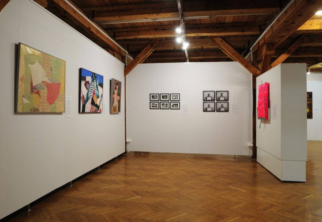Fragment wystawy z obrazami i cyklem fotografii rozmieszczonymi na ścianach w przestrzeni galerii (kliknięcie powiększy zdjęcie).