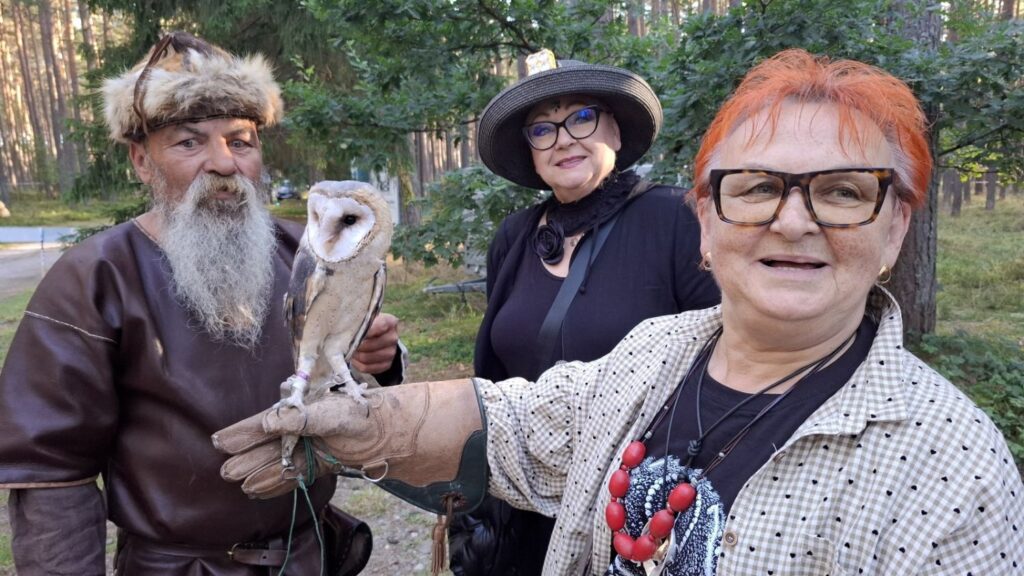 Kobieta trzyma na dłoni sowę; obok stoją osoby w historycznych strojach, a wydarzenie odbywa się w leśnej scenerii (kliknięcie powiększy zdjęcie).