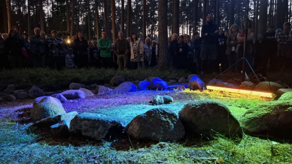 Duże kamienie ułożone na ziemi są oświetlone niebieskim, zielonym i fioletowym światłem. W tle stoi grupa zwiedzających (kliknięcie powiększy zdjęcie).