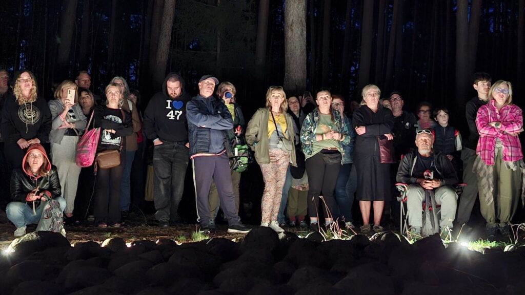 Grupa osób stoi wspólnie na skraju kamiennej instalacji, pozując do zdjęcia; wokół znajduje się ciemny las (kliknięcie powiększy zdjęcie).