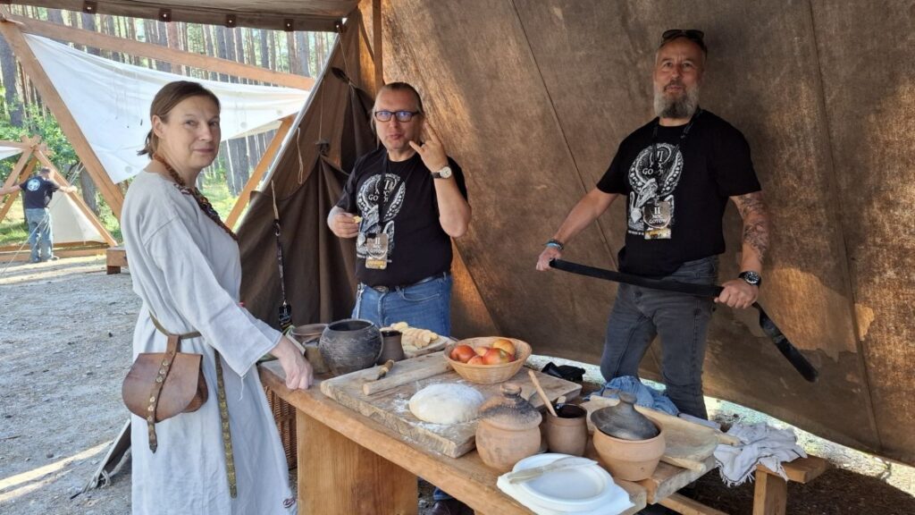 Pracownicy muzeum prezentują stoisko z rekonstrukcjami i przedmiotami nawiązującymi do życia w przeszłości; przy drewnianym stole stoją także osoby w strojach historycznych (kliknięcie powiększy zdjęcie).